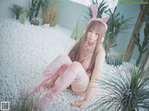 A woman in a pink bunny costume sitting on a bed of white rocks.