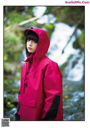 A woman in a red raincoat and white skirt standing in a stream.