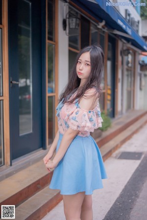 A woman in a blue skirt is standing on the street.