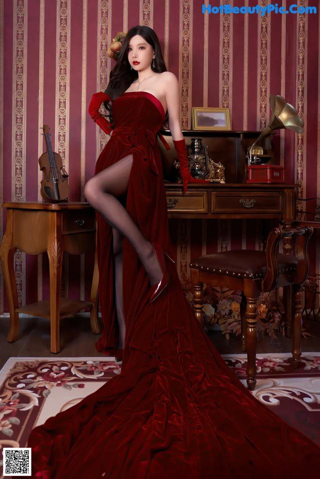 A woman in a red dress posing in front of a piano.