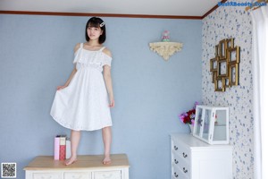 A woman sitting on top of a dresser holding a pink book.