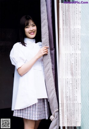 A woman standing in front of a white brick wall holding a book.