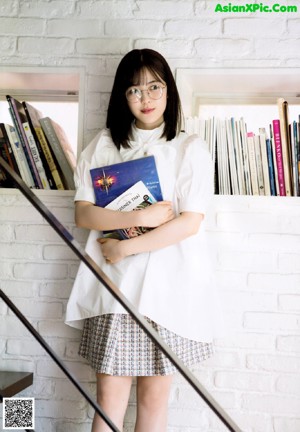 A woman wearing glasses sitting at a table with a book.