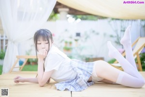 A woman in a white shirt and plaid skirt leaning against a fence.