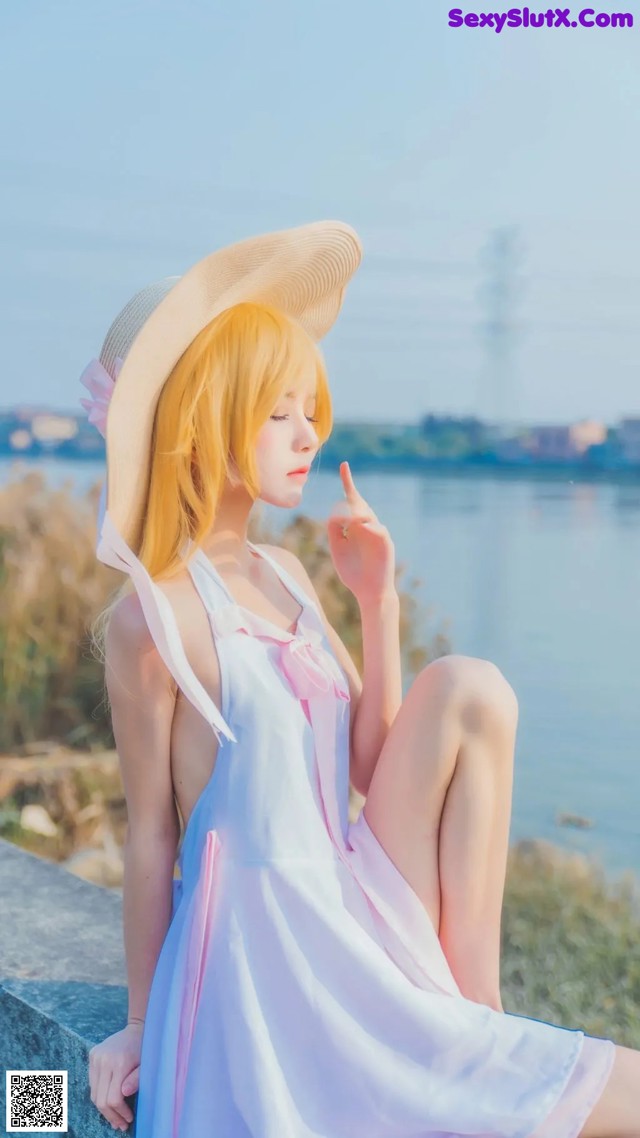 A woman in a white dress and a straw hat sitting on a rock.