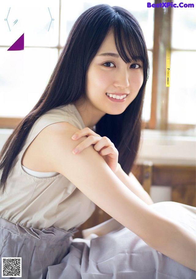 A woman with long black hair sitting in front of a window.