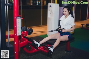 A woman sitting on the floor in a gym with boxing gloves.