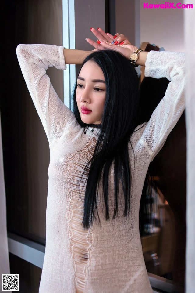 A woman in a white sweater leaning against a window.