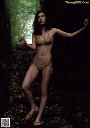 A woman in a bikini standing in the woods.