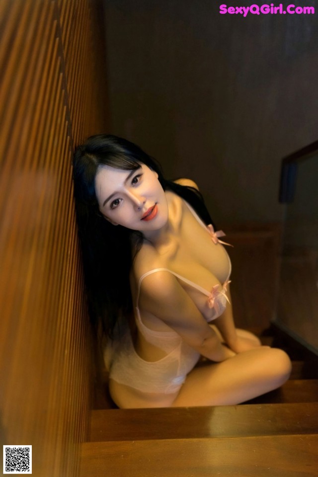 A woman in a white lingerie sitting on a wooden staircase.