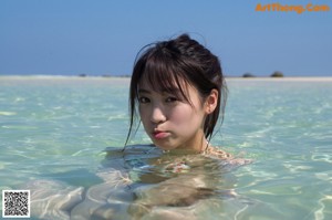 A woman in a bikini sitting on a sandy beach.