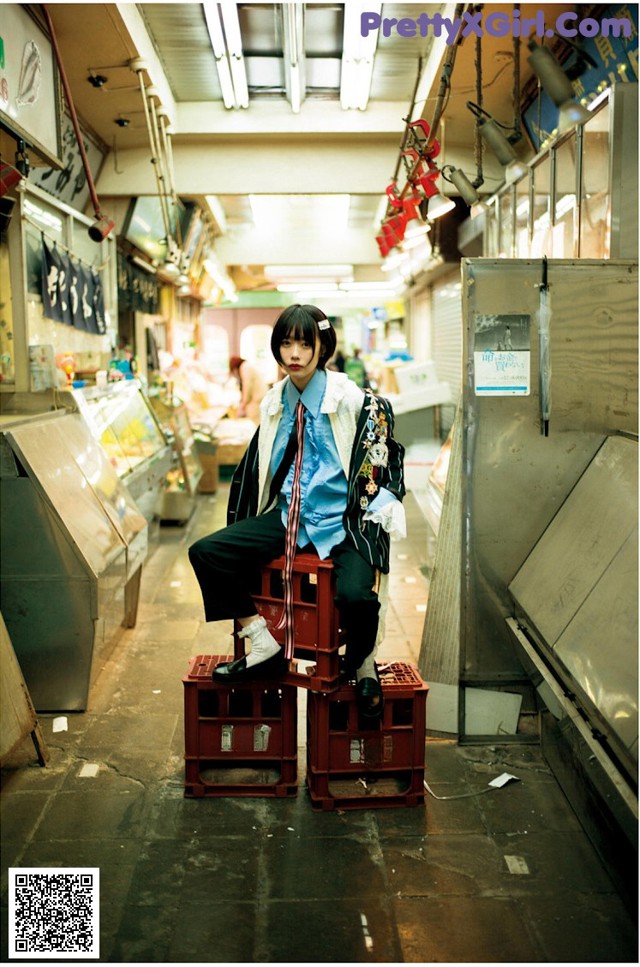 A woman sitting on top of a red crate in a market.