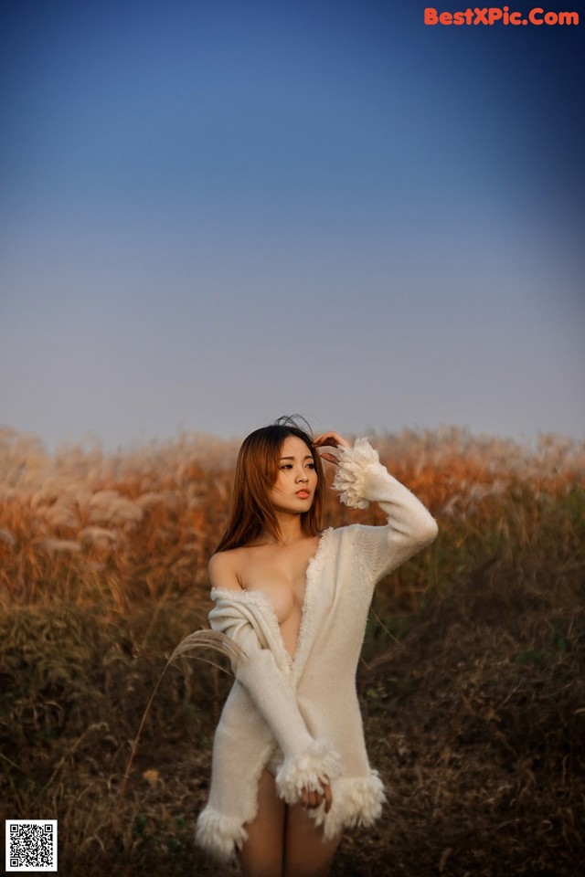 A woman in a white sweater standing in a field.