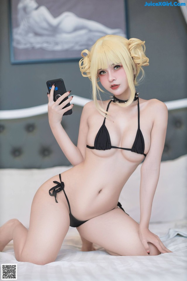 A woman in a black bikini taking a selfie on a bed.