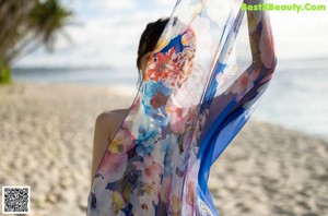 A naked woman standing on a beach next to the ocean.