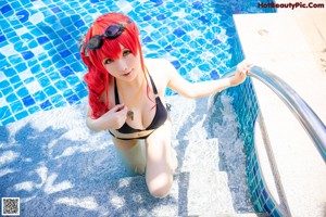 A woman in a black bikini sitting on a ladder by a pool.