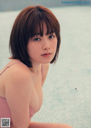 A woman in a pink bikini sitting on the edge of a swimming pool.