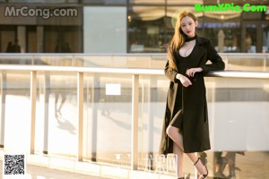 A woman in a black coat leaning against a railing.