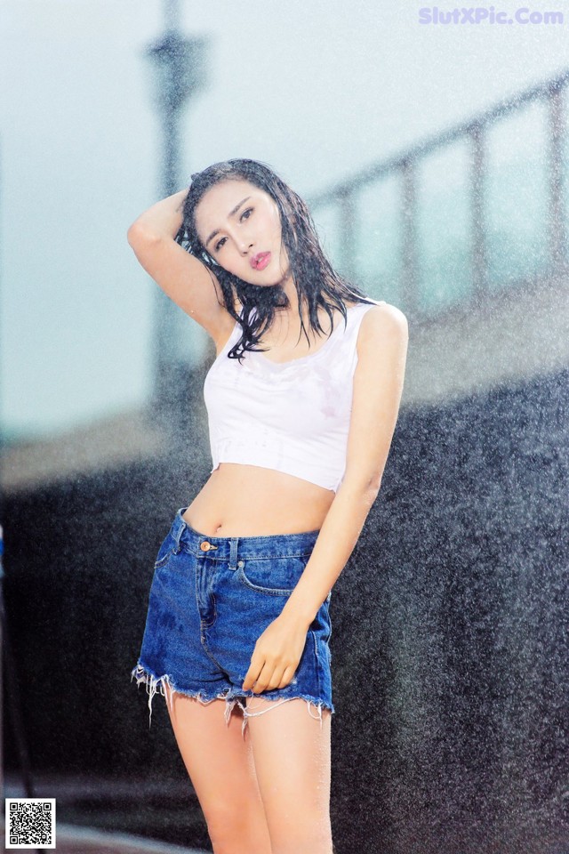 A woman in a white top and blue shorts standing in the rain.