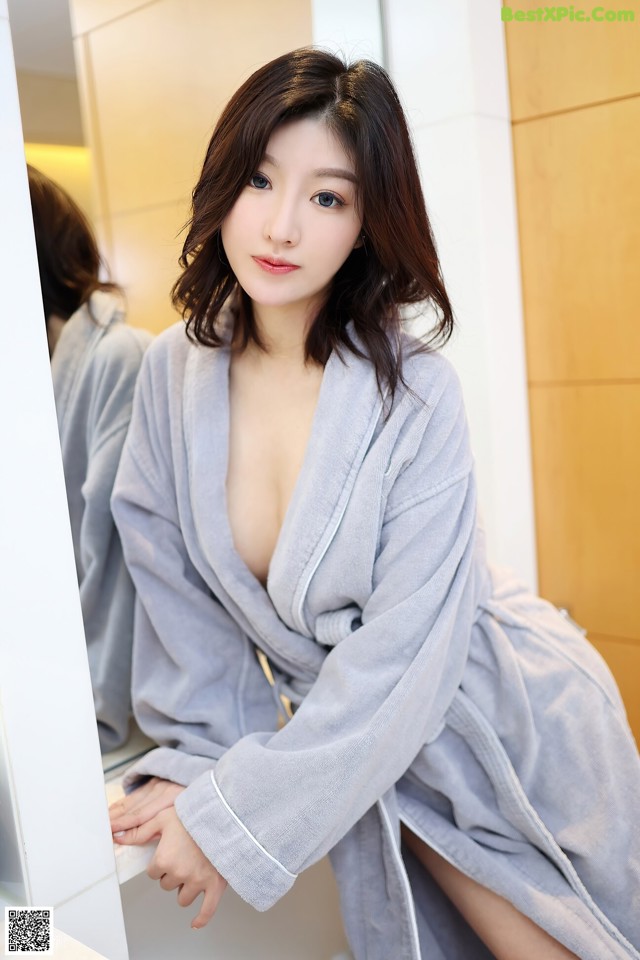 A woman in a bathrobe leaning against a mirror.