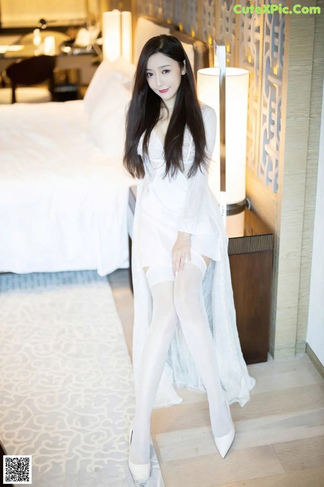 A woman in a white dress sitting on a bed.