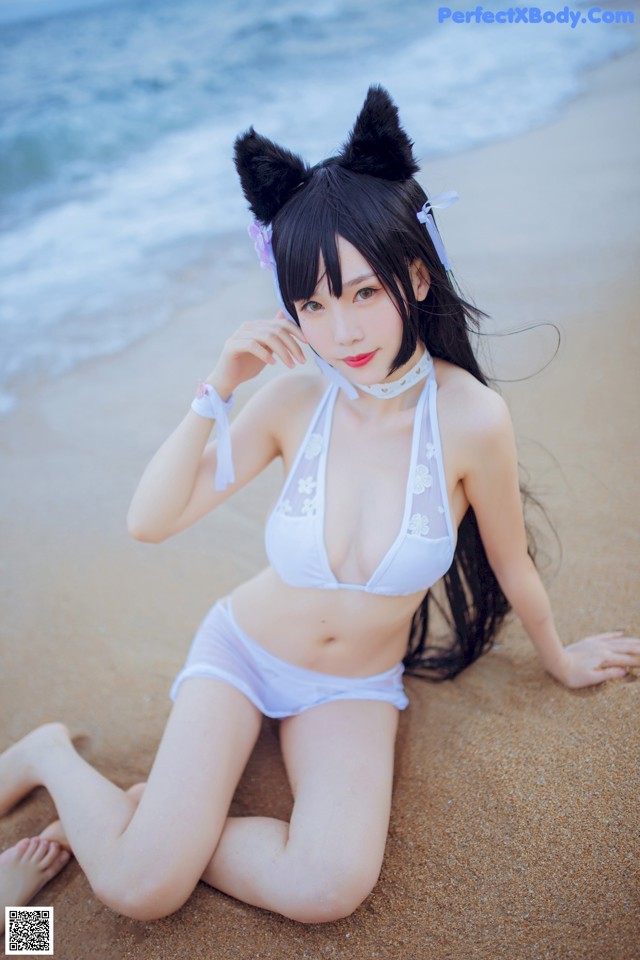 A woman in a white bikini sitting on the beach.