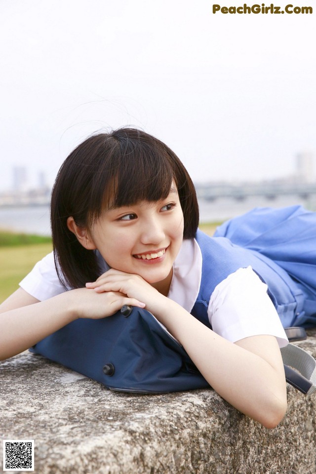 A young woman laying on a stone wall with her hand on her chin.