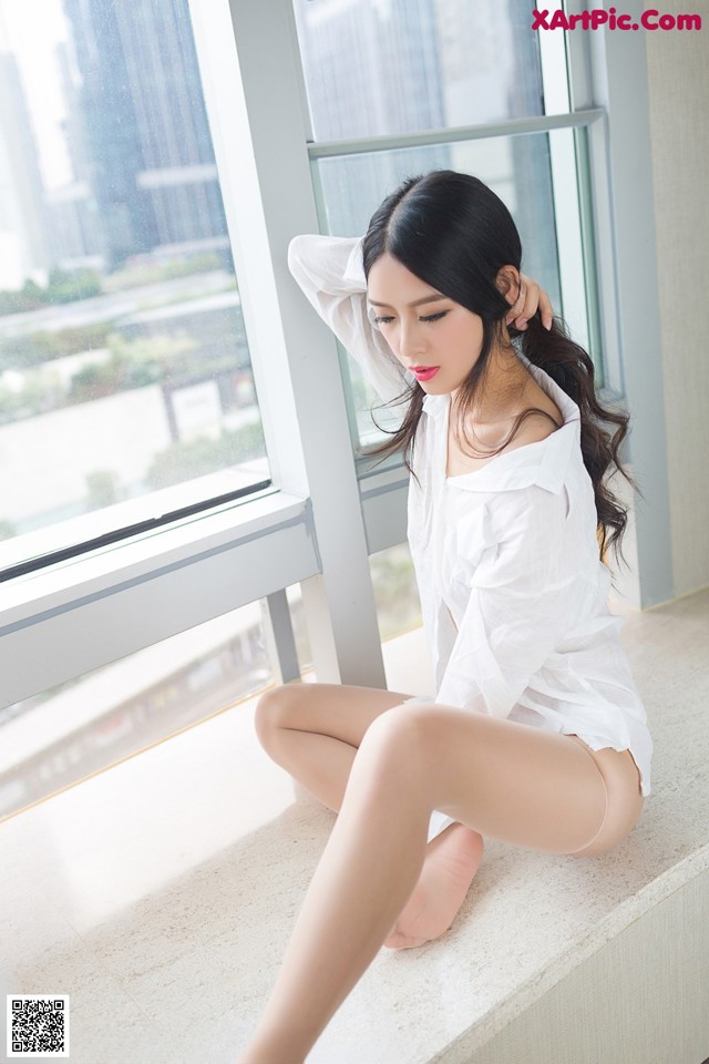 A woman sitting on a window sill in a white shirt.