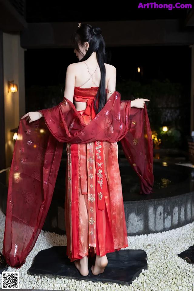 A woman in a red dress standing in front of a fountain.