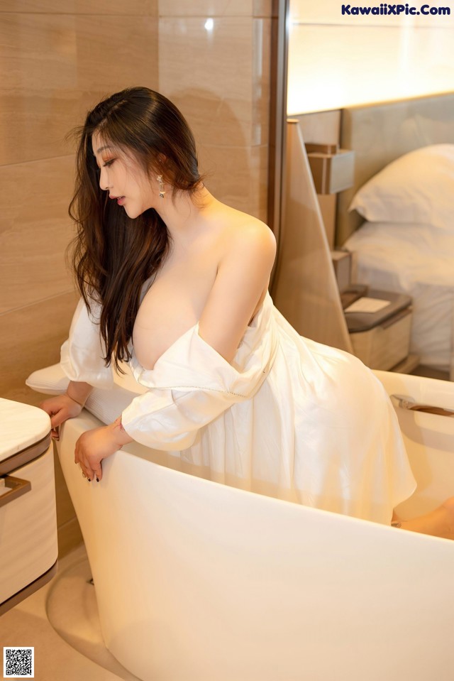 A woman in a white dress sitting in a bathtub.