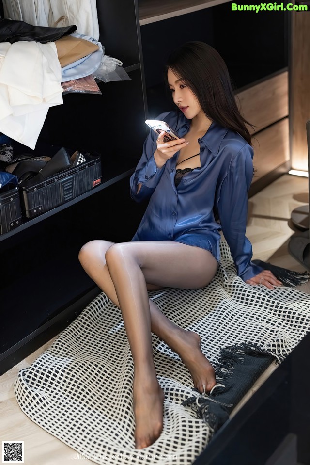 A woman sitting on a bed looking at her phone.