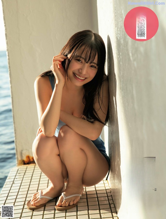 A woman sitting on the edge of a wall next to the ocean.