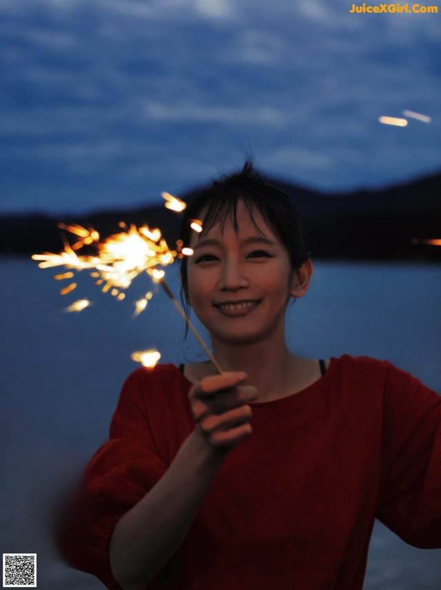 A woman holding a sparkler in front of a lake.
