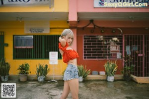 A woman in a red top and denim shorts posing for a picture.