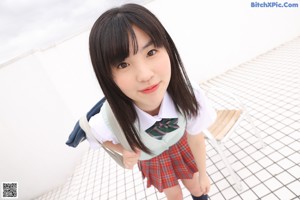 A young woman in a school uniform sitting on a bed.