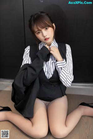 A woman in a black vest and white shirt is sitting on the floor.