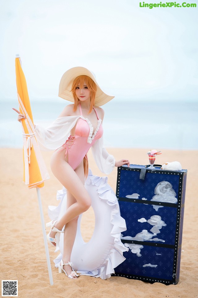 A woman in a pink bathing suit and hat on the beach.