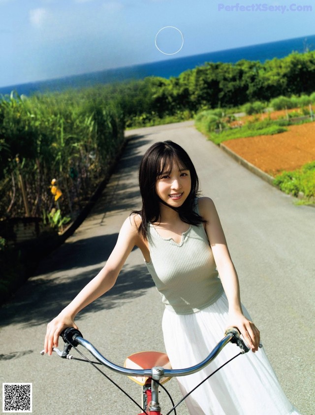 A woman riding a bike down a road next to the ocean.