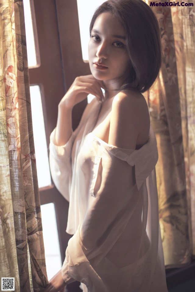 A woman in a white dress leaning against a window.