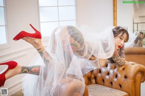 A woman with tattoos sitting on a couch wearing a veil.