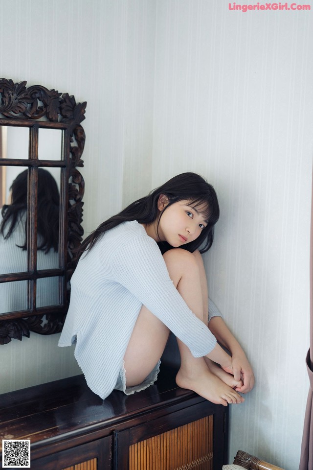 A woman sitting on top of a dresser next to a mirror.