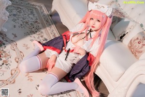 A woman with long pink hair sitting on a bed.